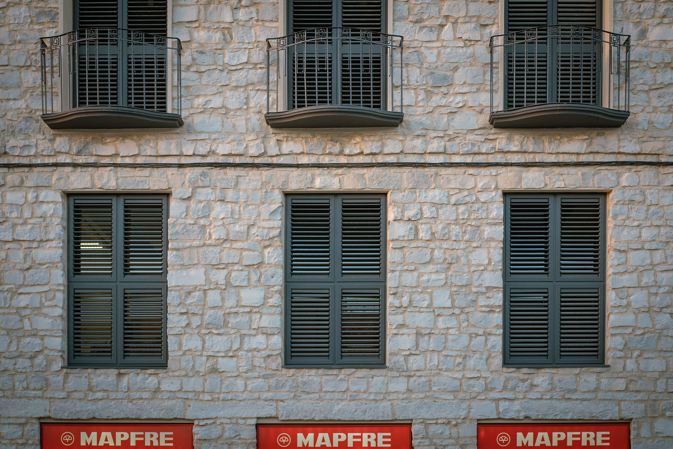 Alzado frontal de la fachada de piedra con tres balcones en planta primera y ventanales en planta baja